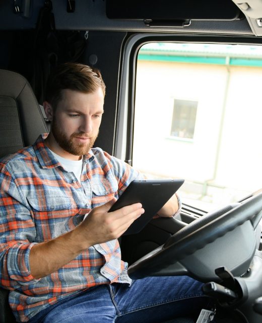 Man truck driver sitting behind wheel of car and holding digital tablet in his hands.